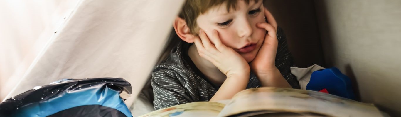 Klein jongen leest een boek in bed, met een pakje dryites aan de linkerkant