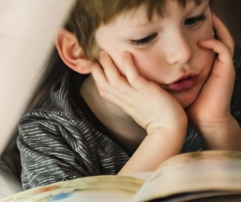 Klein jongen leest een boek in bed, met een pakje dryites aan de linkerkant.